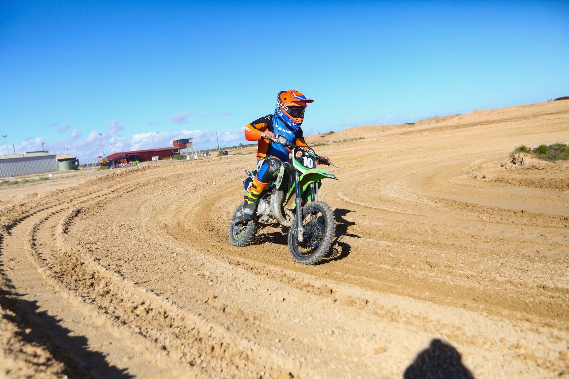 Young rider railing a berm on a green dirt bike under a big blue sky